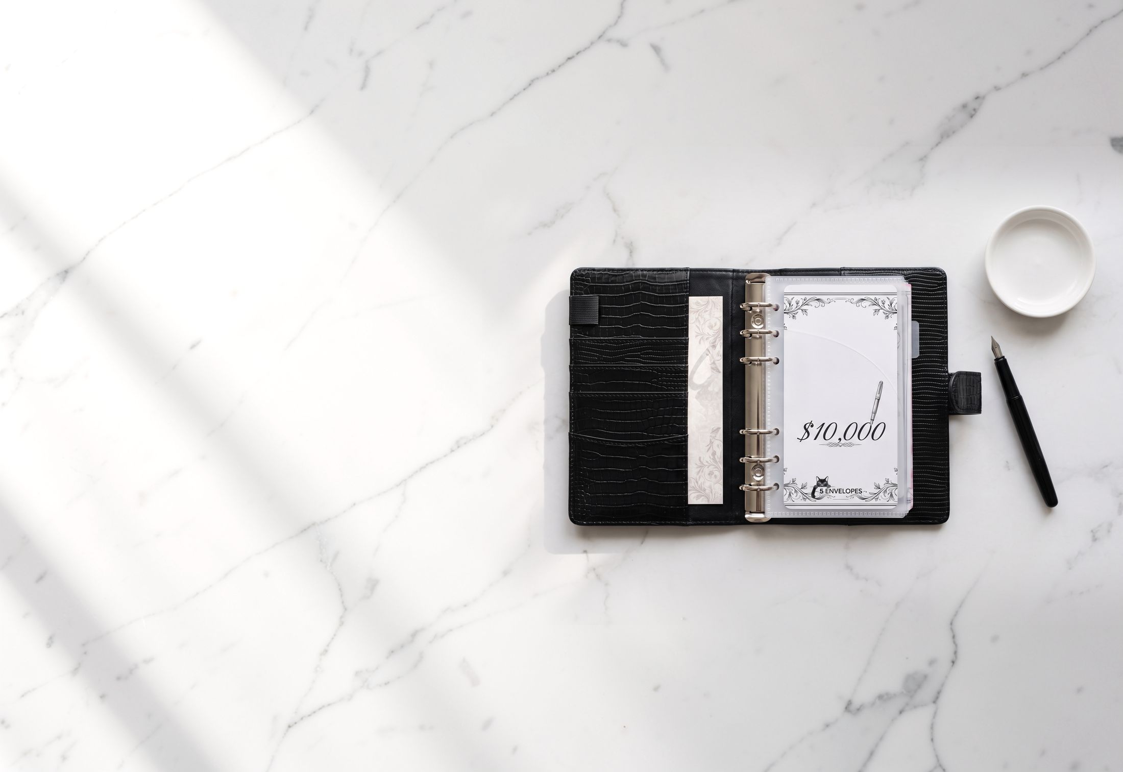 A black budget binder holding a $10,000 savings card on white marble